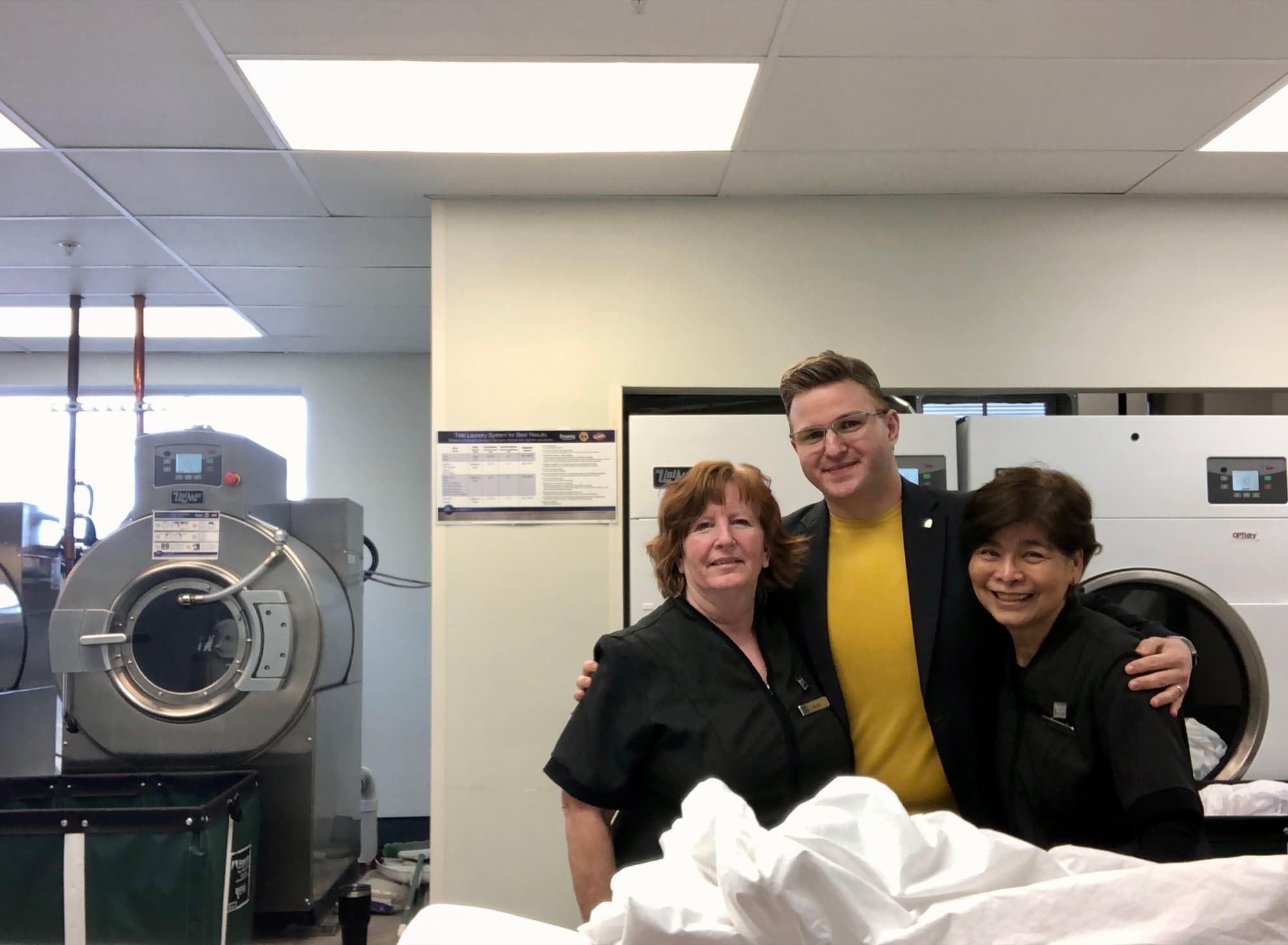 Curtis in a suit in a hotel laundry room, arms around two colleagues