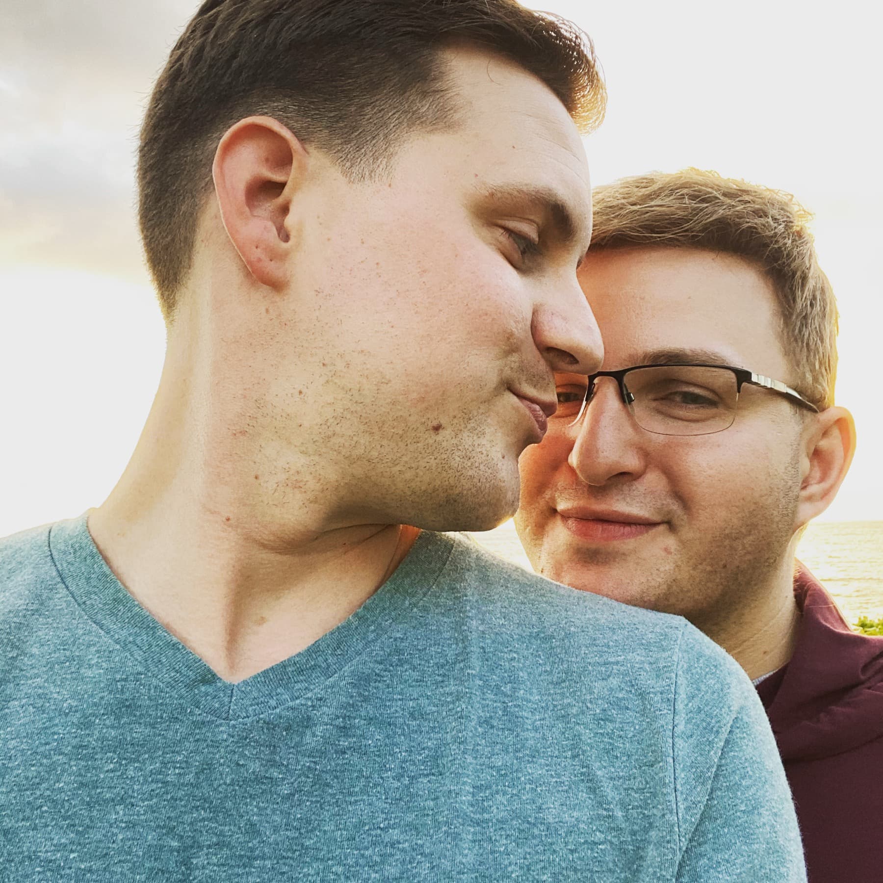 Michael kissing Curtis on the cheek at sunset by the water