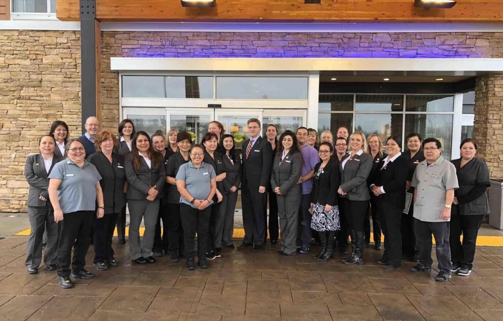 A hotel team of about thirty people in uniform in front of the entrance, Curtis in a suit at the center